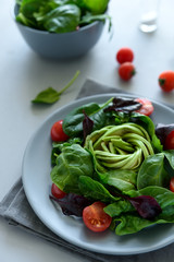 Salad mix with avocado, spinach, tomatoes and beet leaves on gray wooden background. Vegetarian food concept. Selective focus.