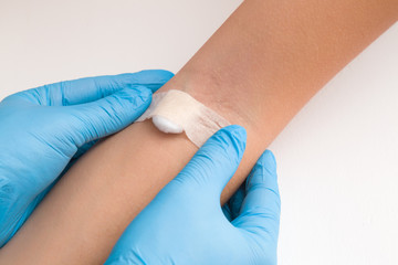 Doctor in blue rubber protective gloves putting an adhesive bandage on young woman's arm vein after blood test or injection of vaccine. First aid. Medical, pharmacy and healthcare concept. Closeup.