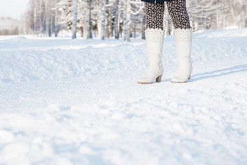 Fototapeta na wymiar Young woman's legs in white, leather boots walking on snowy forest trail after blizzard. Enjoying stroll in sunny, chilly day. Footwear for daily walking in winter season.
