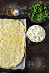 Recipe cooking pizza with spinach and feta. Raw pizza dough on a sheet for baking. Bowls with chopped spinach and feta pieces. View from above. Keto recipe idea.