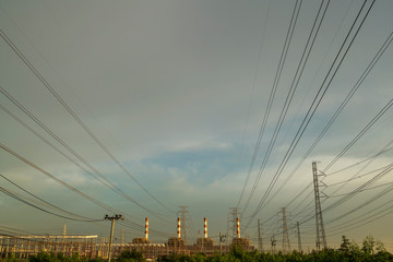 Many high voltage power pole and cable lines with smokestack of power plant in back with beautiful...