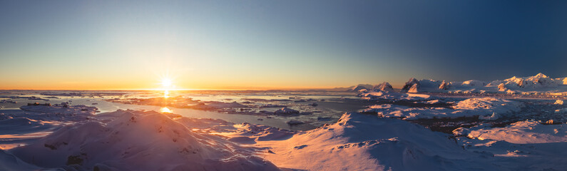 Bright colorful sunset panorama view in Antarctica Ocean. Orange sun lights over the snow covered polar surface. Picturesque winter landscape. The beauty of the wild untouched Antarctic nature.