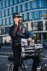 Male courier with bicycle delivering packages in city, making a phone call.