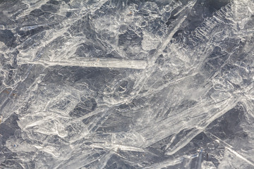 Cracked ice on the frozen surface of the lake. Winter patterns on ice water