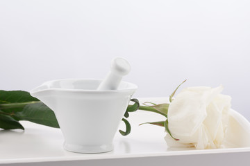 White mortar, pestles and white rose flower on wooden tray isolated on white background.