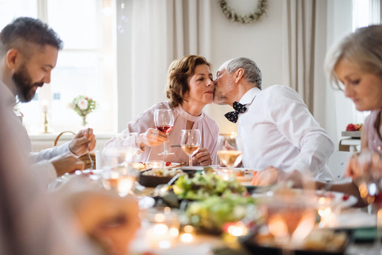 A senior couple sitting at a table on a indoor birthday party, kissing.