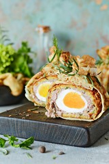 Scotch eggs in a pancake bag with greens on a gray-blue background. A classic dish in an unconventional serving. Delicious and appetizing dish of British cuisine.