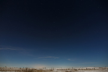 Stars in the night sky over the snow-covered plain. The background of deep space is photographed under the full moon.
