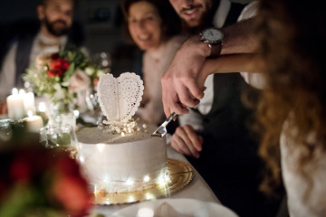 A midsection of young couple sitting at a table on a wedding, cutting a cake.
