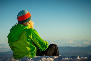 Junge Frau sitzt im Schnee und betrachtet die Berge