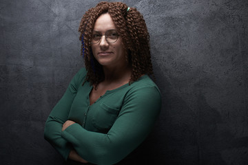 Portrait of an authentic adult woman with afro curls against a black wall in the studio. Unusual stylish woman with red hair