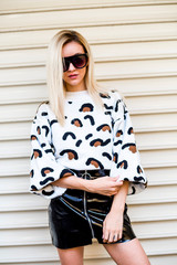 Portrait of young woman in stylish clothes and sunglasses in front of wall