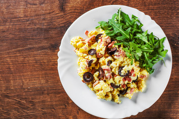 scrambled eggs with ham, olive and arugula salad in white plate on wooden table background