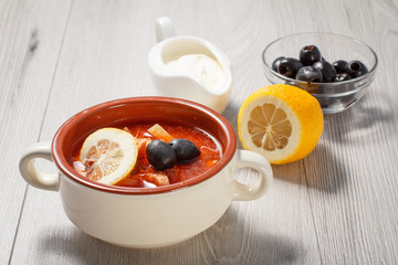 Soup saltwort with meat, potatoes, tomatoes, lemon, black olives and sour cream in ceramic bowl.