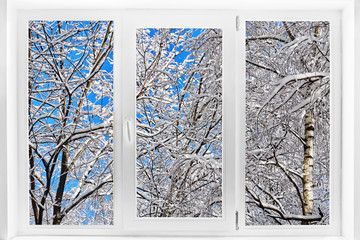 Plastic window with a winter view with tree branches covered with snow on blue sky background