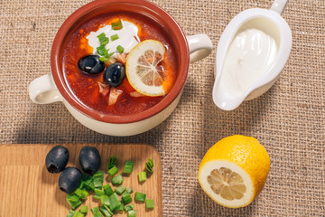 Soup saltwort with meat, potatoes, tomatoes, lemon, black olives and sour cream in ceramic soup bowl.