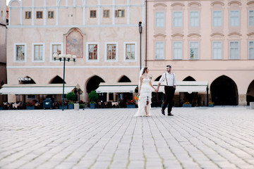 Obraz premium Romantic wedding couple of groom and bride walking holding hands on the beautiful old streets of Prague city. Czech Republic