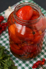 Marinated tomatoes with a viburnum in a open jar are located on a dark background