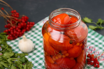 Marinated tomatoes with a viburnum in a open jar are located on a dark background