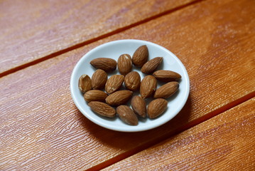 Top view of almonds nuts in white bowl on wooden background.