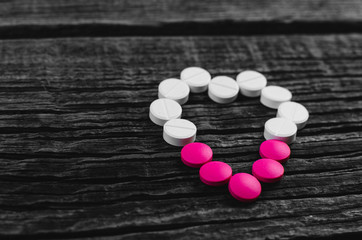 heart made of pink and white pills on wooden surface