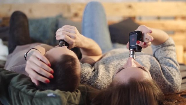 A loving couple on a bed smokes electronic cigarettes.