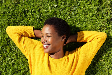 above of happy young black woman lying on green grass