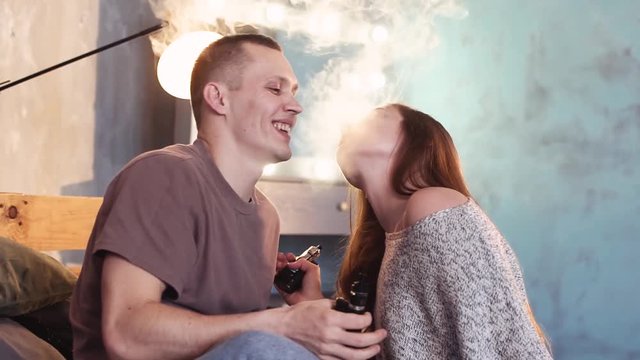 A loving couple on a bed smokes electronic cigarettes.