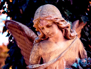 A fragment of ancient sculpture angel in a golden glow in the old cemetery. Symbol of love,...