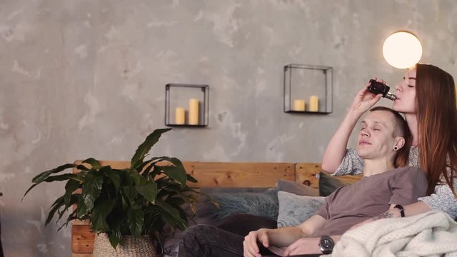 A loving couple on a bed smokes electronic cigarettes.