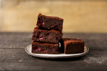 Brownie dessert slices with cherry on a plate, wooden background