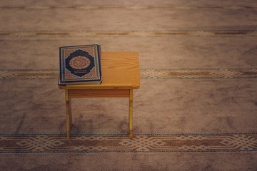 Koran Islamic religion book object on prayer place in mosque interior soft brown carpet environment, copy space