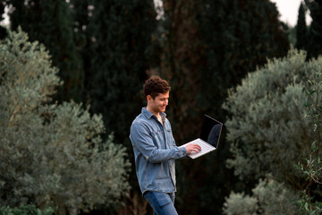 Fototapeta premium Man in jeans suit standing with a laptop in garden with mandarins