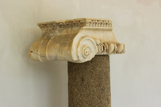 Greek antique column exhibit object on white wall background, museum sightseeing concept photography