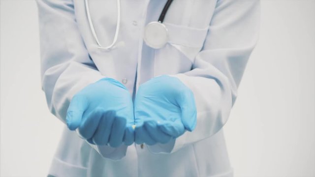 A beautiful young doctor doctor dressed in a white robe and blue gloves. During this time it is on a gray background and puts the tablets in the close-up.