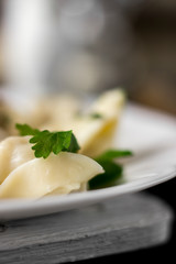 Traditional russian pelmeni, ravioli, dumplings with meat on dark concrete background. Parsley, pepper, and spices.
