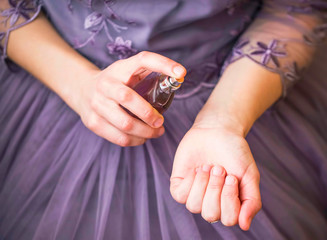 Woman in elegant purple dress applying perfume on her wrist closeup, selective focus