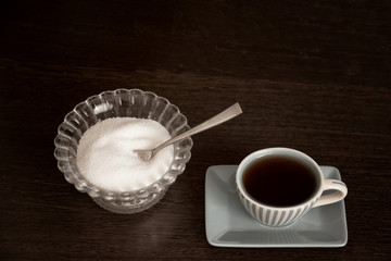 A Cup of strong tea and sugar in a sugar bowl on a dark wooden table.