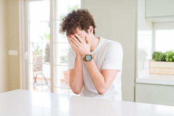 Fototapeta premium Young handsome man wearing white t-shirt at home with sad expression covering face with hands while crying. Depression concept.