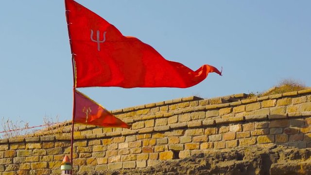 Red flag of a hindu temple fluttering in the wind over the stone wall of a temple in Diu near INS Khukri point