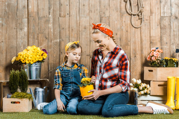 daughter looking at flowers in hands of cheerful mother while sitting near wooden fence
