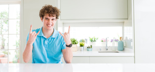 Fototapeta na wymiar Wide shot of young handsome man at home shouting with crazy expression doing rock symbol with hands up. Music star. Heavy concept.