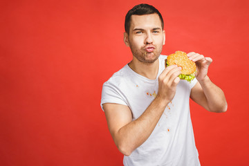 Funny hungry bearded man eating junk food. Excited young man greedily eating hamburgers isolated on...