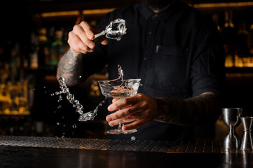 Bartender adding to an alcoholic drink in the glass an ice cube