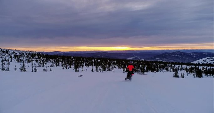 the snowmobile passes to the right of the camera, looks into the frame and quickly rides a snowmobile in a beautiful mountain valley at sunrise. drone's coming. stock video footage. Aerial drone shot