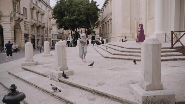 A mother with a baby sling feeds doves in the old town Valetta in slow motion