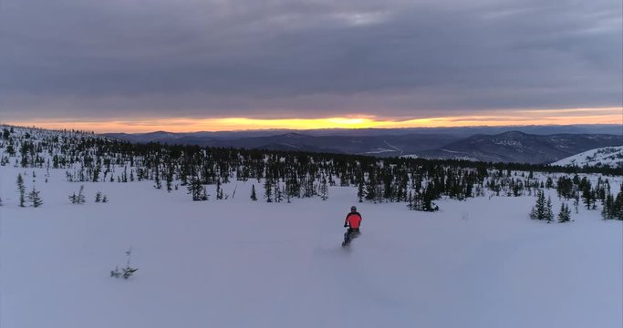the snowmobile passes to the right of the camera, looks into the frame and quickly rides a snowmobile in a beautiful mountain valley at sunrise. drone's coming. stock video footage. Aerial drone shot