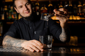 Smiling bartender adding to an alcoholic drink in the glass a big ice cube