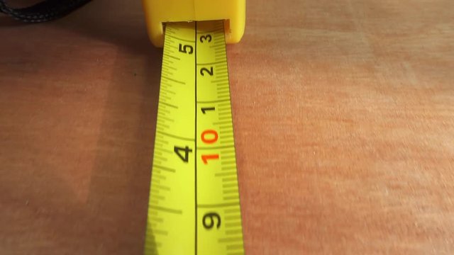 Measurement with a tape measure.  Track along as a steel tape measure extends over a sheet of timber.