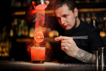 Fototapeta na wymiar Tattooed man adding to an alcoholic cocktail a dried orange and powder